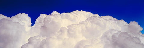 View from a plane of white puffy clouds in front of a deep blue sky 