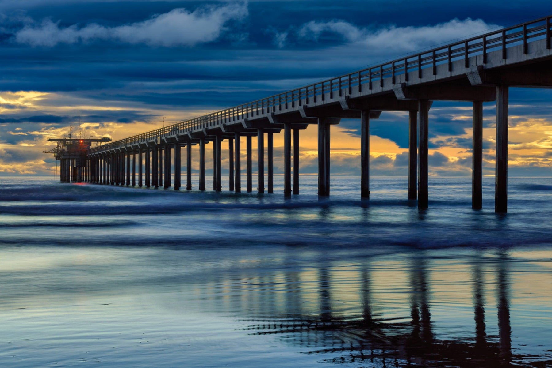 Scipps Pier in California leading off into the ocean under a blue and stormy sky