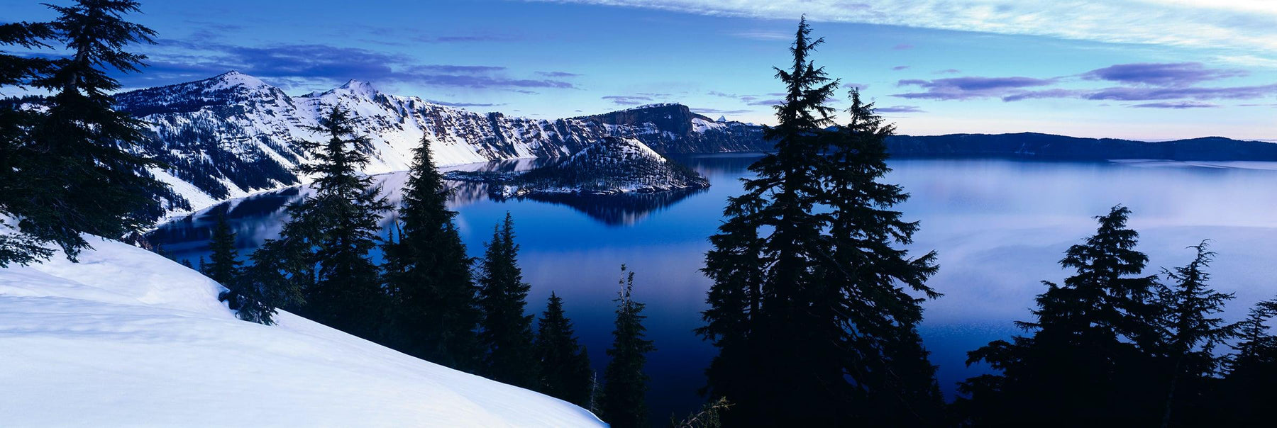 View of Crater Lake Oregon looking over pine tree silhouettes from the snow covered mountainside 