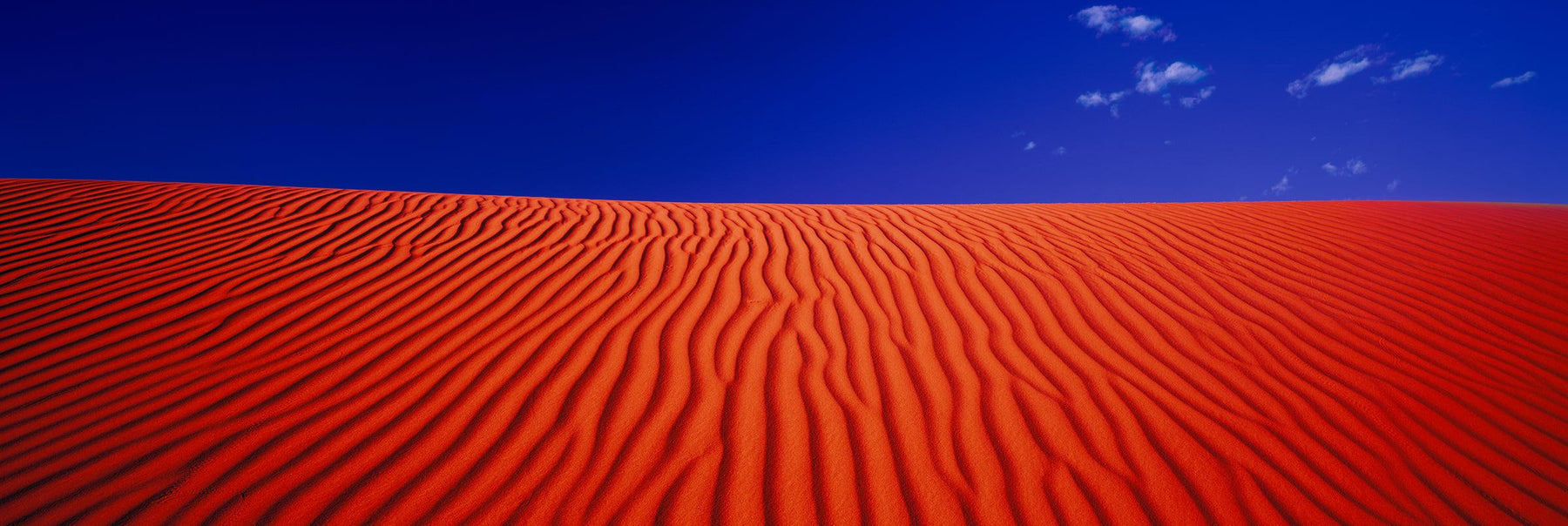 Bright orange windswept sand dunes of Simpson Desert Australia with a blue sky above