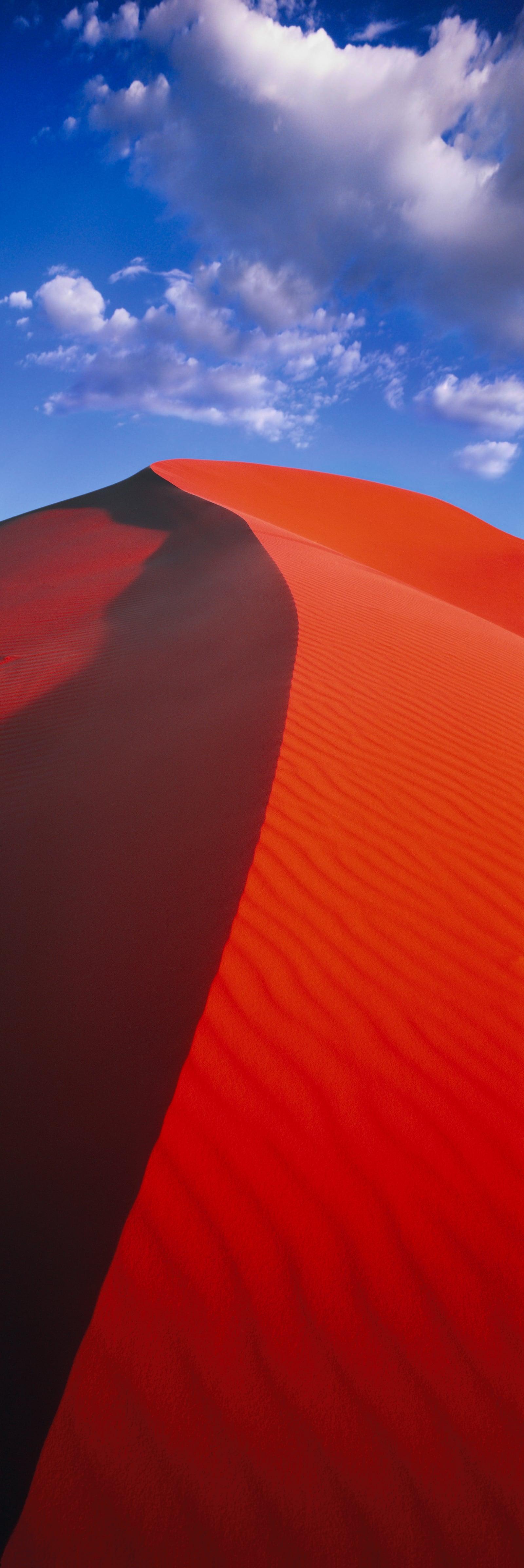 Red windswept sand dunes under cloudy blue skies in Coral Pink Sand Dunes Utah