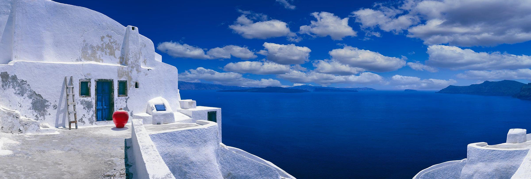 White plastered house and courtyard overlooking the blue ocean and cloudy skies of Santorini Greece