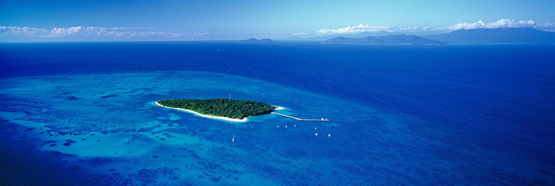 Aerial view of Green Island full of trees with a pier and boats surrounded by the Great Barrier Reef Australia