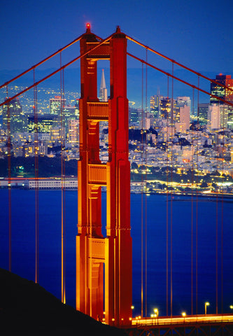 Close up of one of the Golden Gate Bridge towers at night with San Francisco lit up in the background