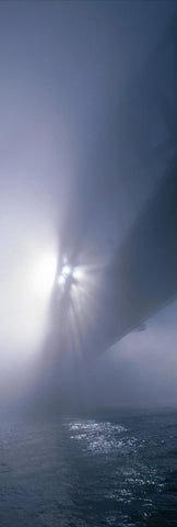 Sun shining through the mist covered Sydney Harbour Bridge with water below 