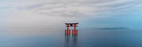 Red Torii gate standing in a calm blue lake in Japan with hills in the background