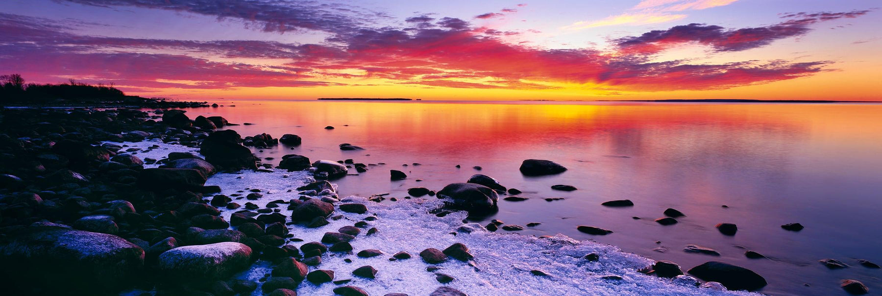 Snow covered rock beach of Lake Superior Michigan during a cloudy sunset