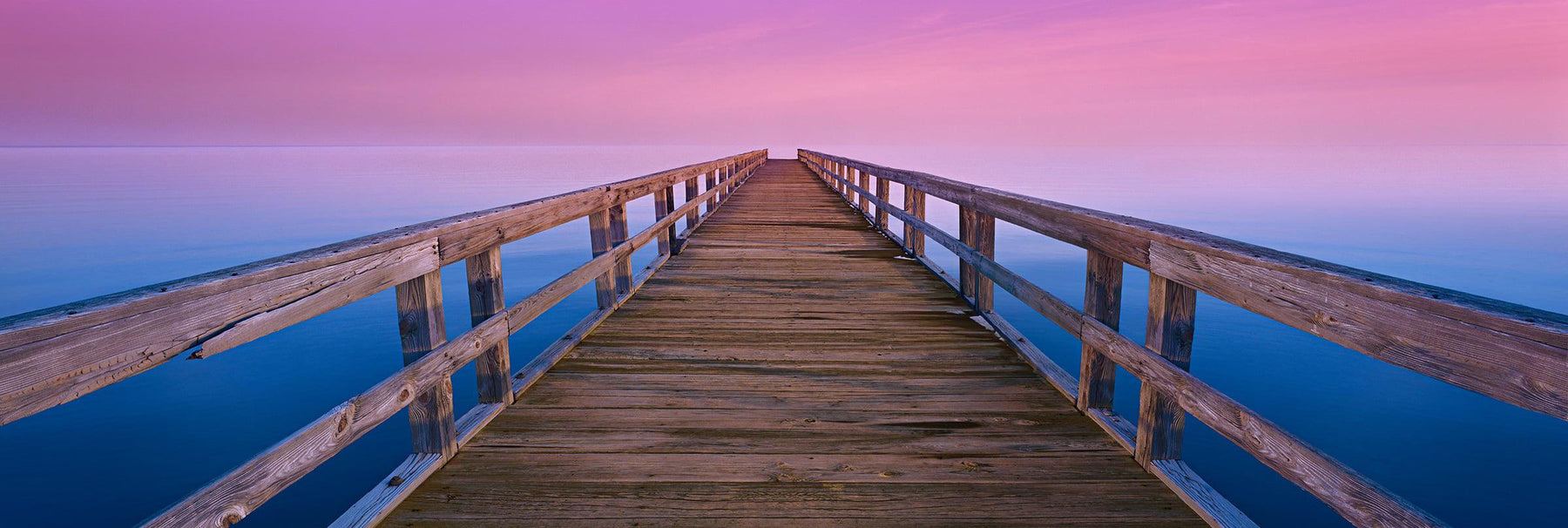 Old wooden pier reaching over the ocean into a pink and purple horizon during a sunrise in Port Mahon Delaware
