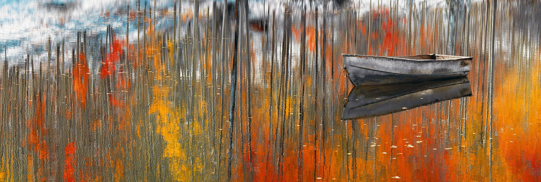 Old metal row boat floating on a lake in Aspen Colorado with the Autumn forest reflecting in the water