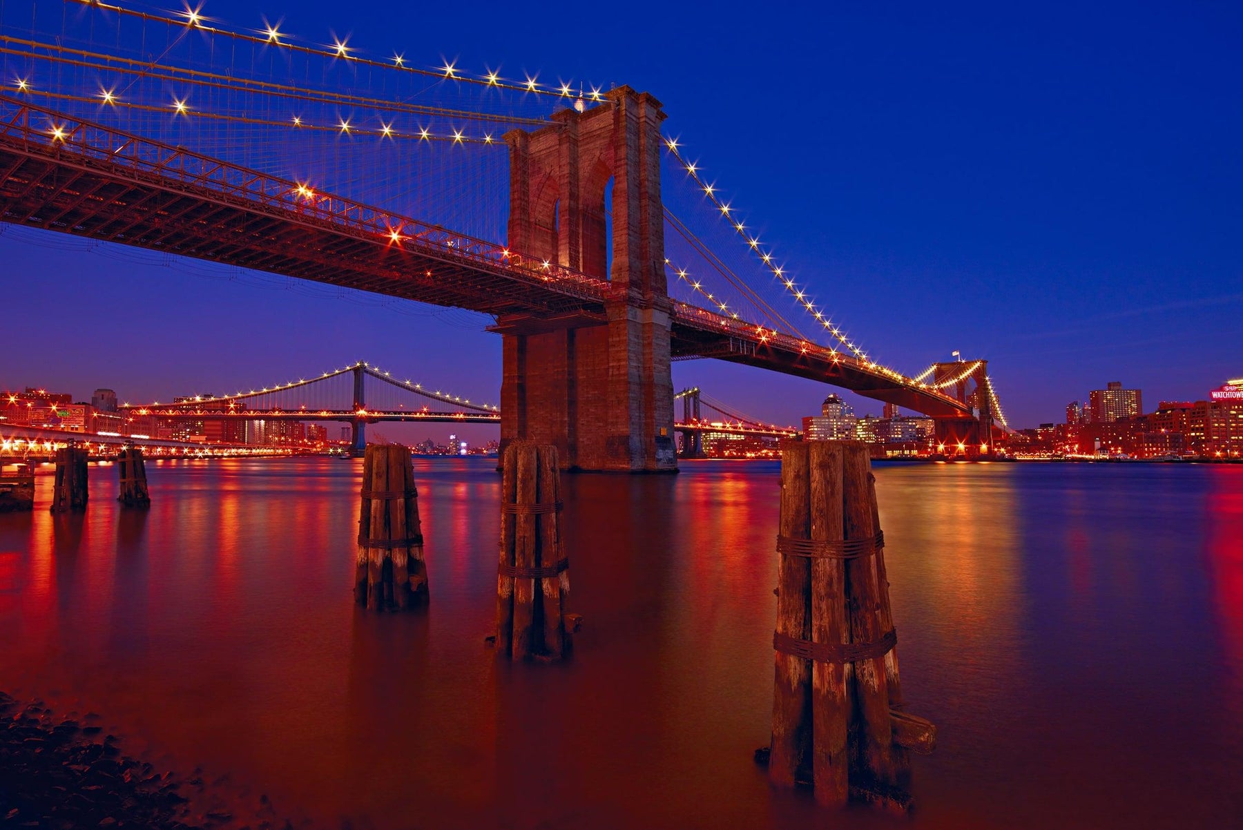 Brooklyn Bridge lit up at night from the waters edge with the Manhattan Bridge and New York City in the background
