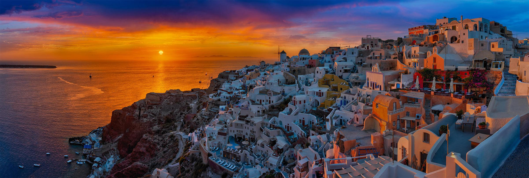White and orange buildings along the cliffs of Santorini Greece with the sun setting over the ocean behind