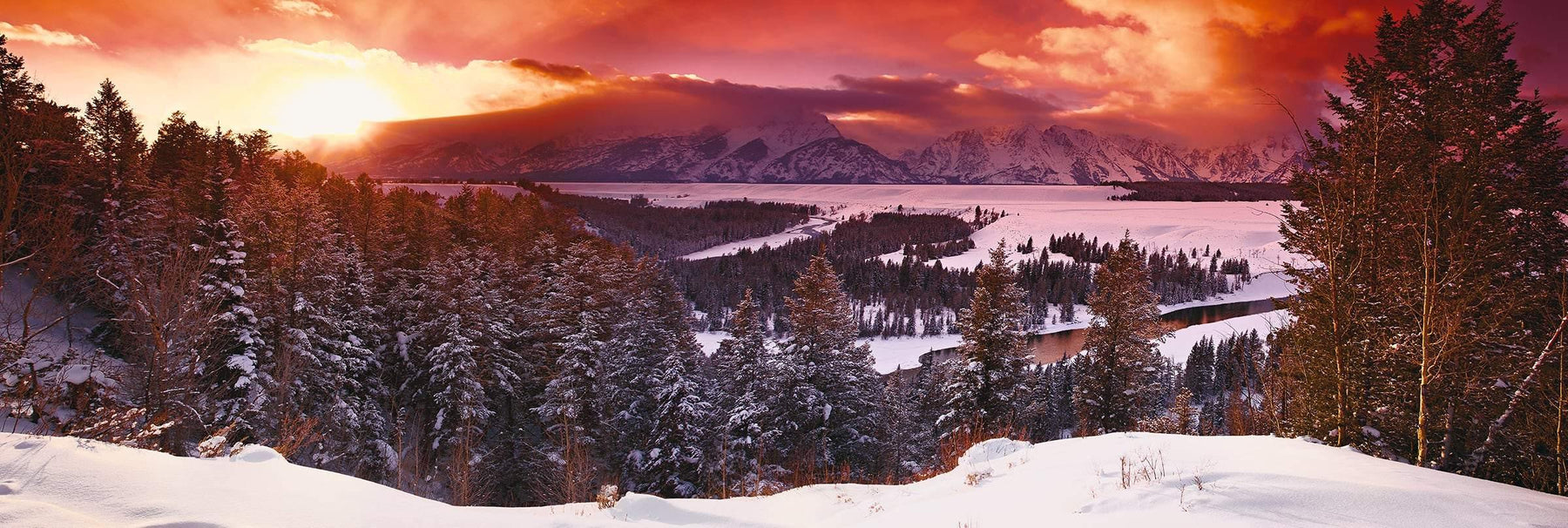 Sun shining through the clouds as it sets on the snow covered valley and forest of Grand Tetons National Park Wyoming