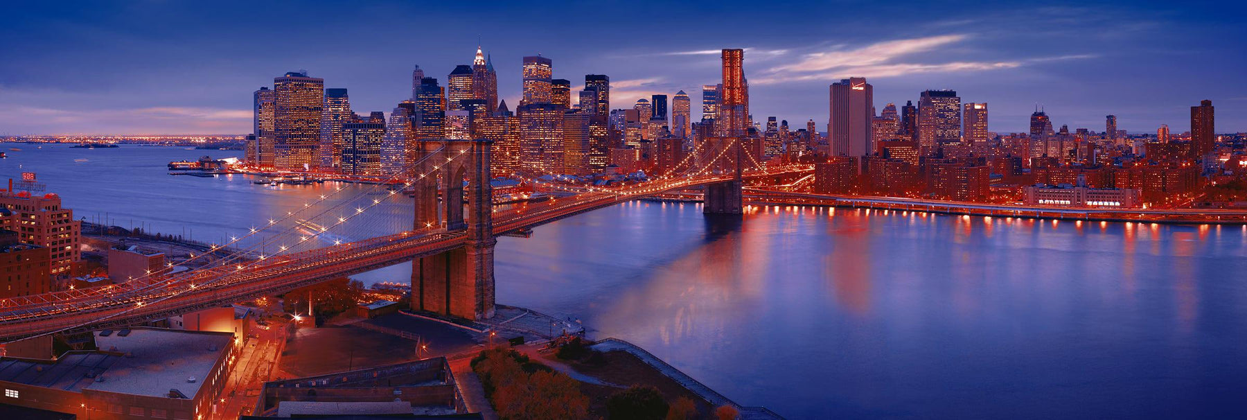Rooftop view of New York and the Brooklyn Bridge lit up at twilight reflecting on the East River