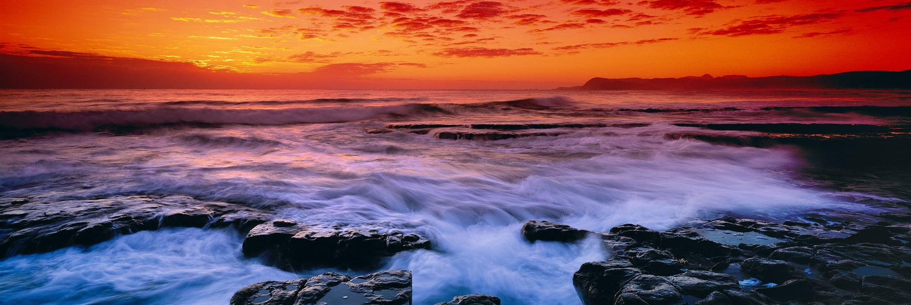 Waves crashing during sunrise off a rocky beach in Tasmania at sunset
