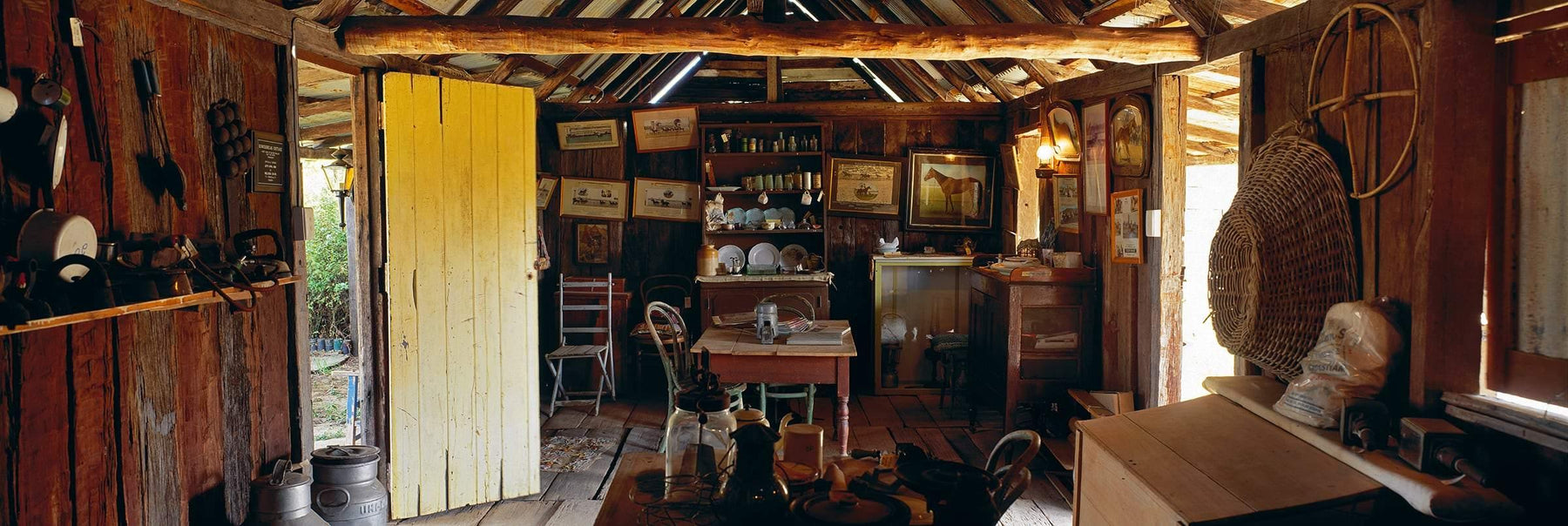 Interior of an old wooden shack filled with framed pictures table and chairs dishes and other miscellaneous items