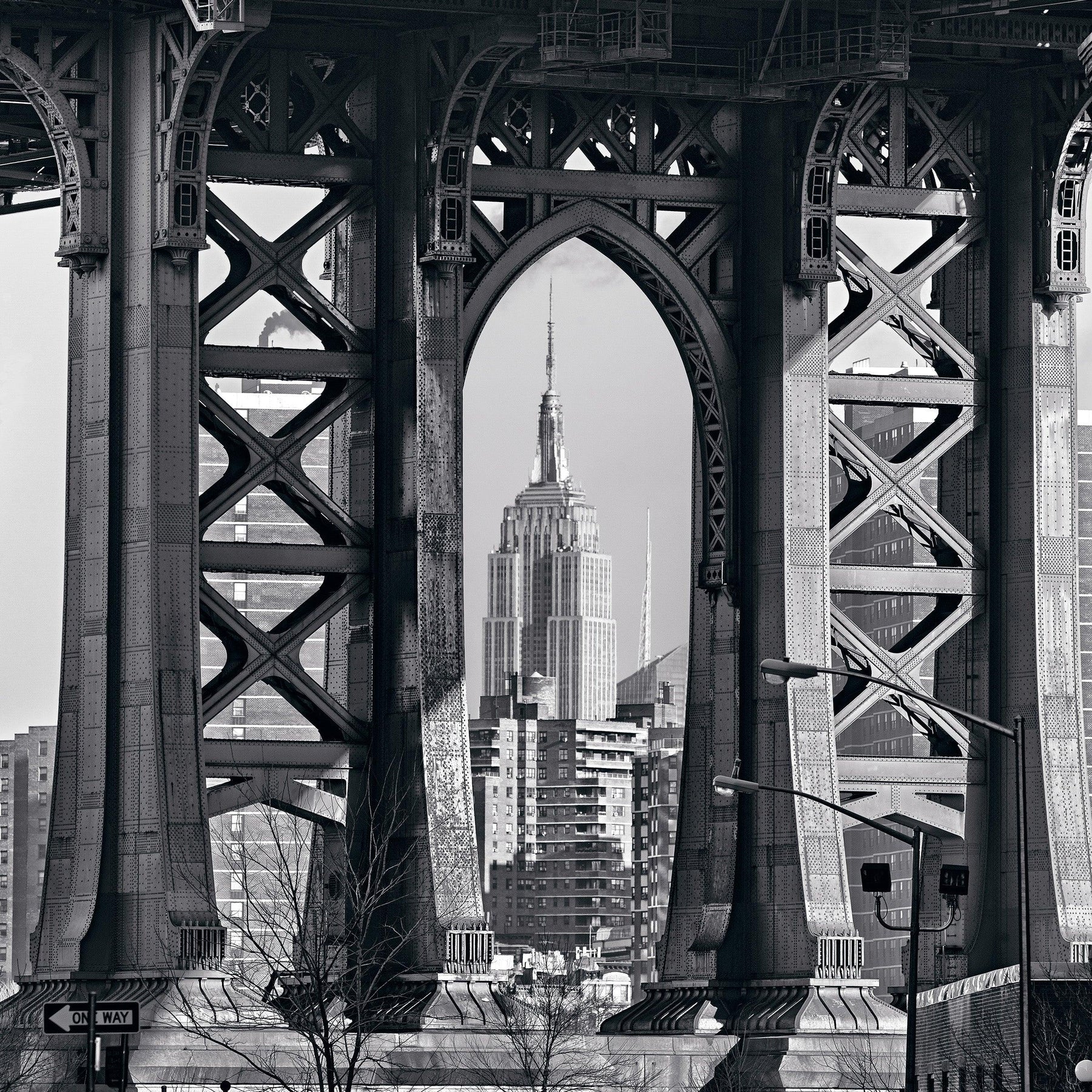 Black and white of the Empire State Building framed within the arches under the Manhattan Bridge New York