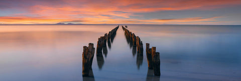 Remains of an old wooden jetty leading into a bay in Victoria Australia at sunset