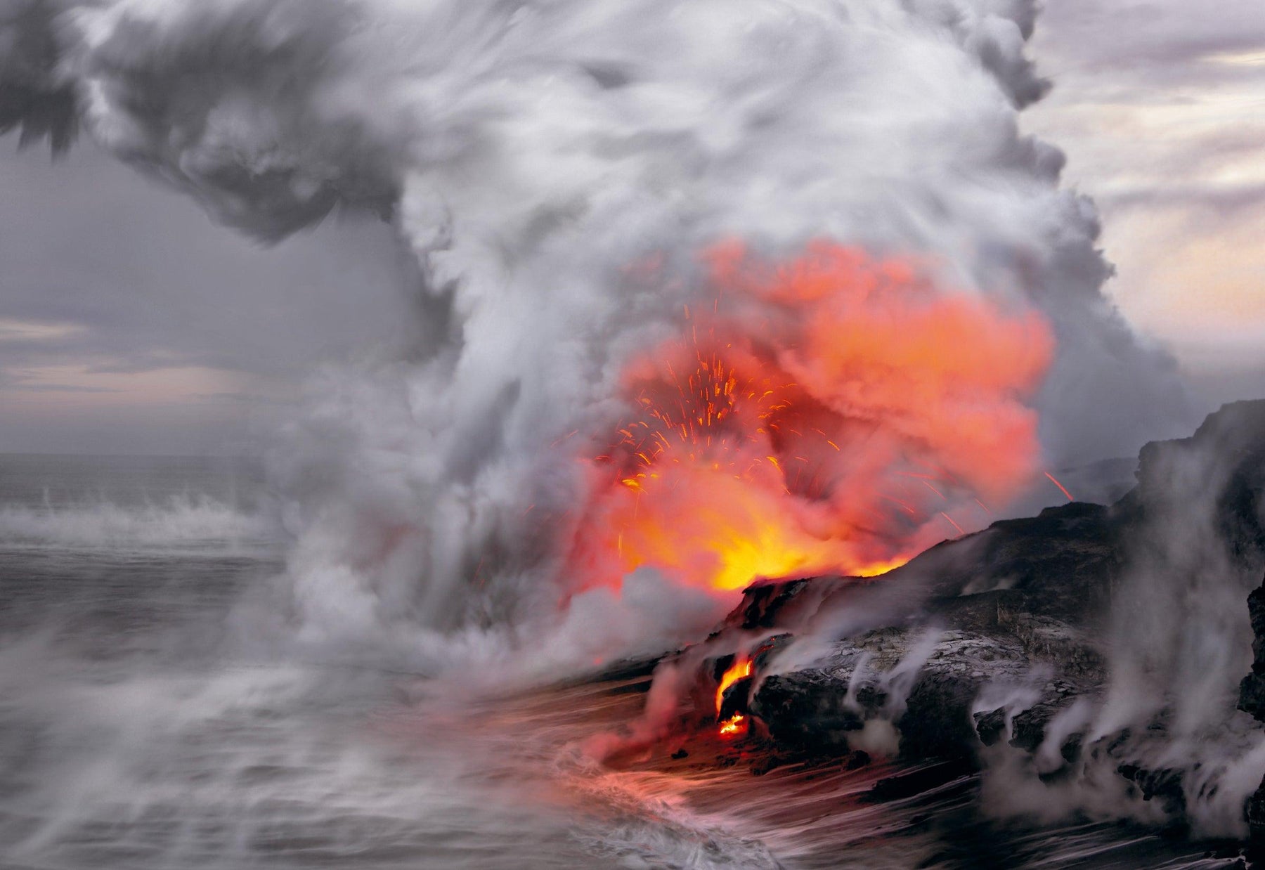 Fire and lava hitting the ocean water creating a giant cloud of steam and smoke on the shoreline of Kilauea Hawaii