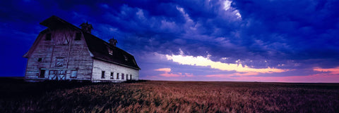 Weathered old white barn in the middle of a wheat field in North Dakota as a storm rolls in
