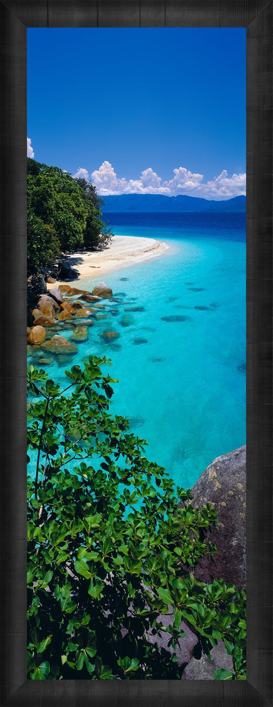 Foliage on the edge of a rock ledge looking down at the white sand beach with a dark brown frame