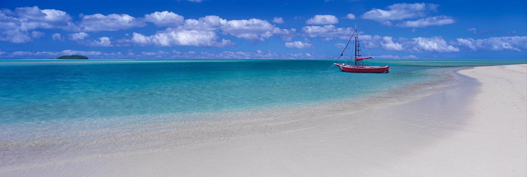 Red sail boat floating in the turquoise ocean just off a white sand beach in the Great Barrier Reef of Australia