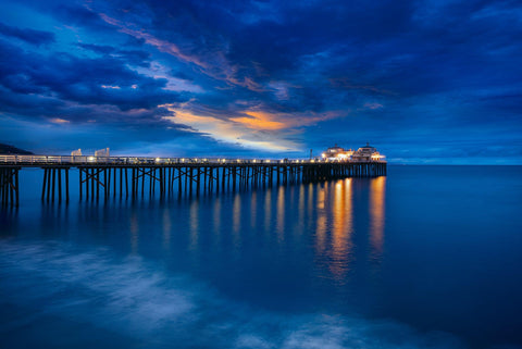Malibu Pier leading out over the ocean in California lit up at night under a cloud filled sky