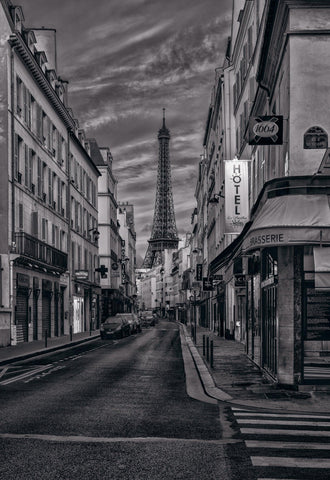 Black and white city street in Paris France with cars and buildings in front of the Eiffel Tower and a cloud filled sky
