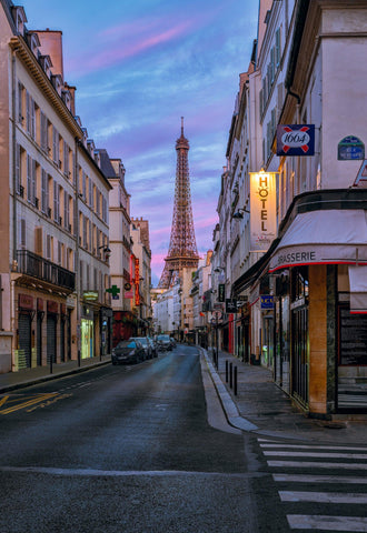 City street in Paris France with cars and white buildings in front of the Eiffel Tower and a pink cloudy sky