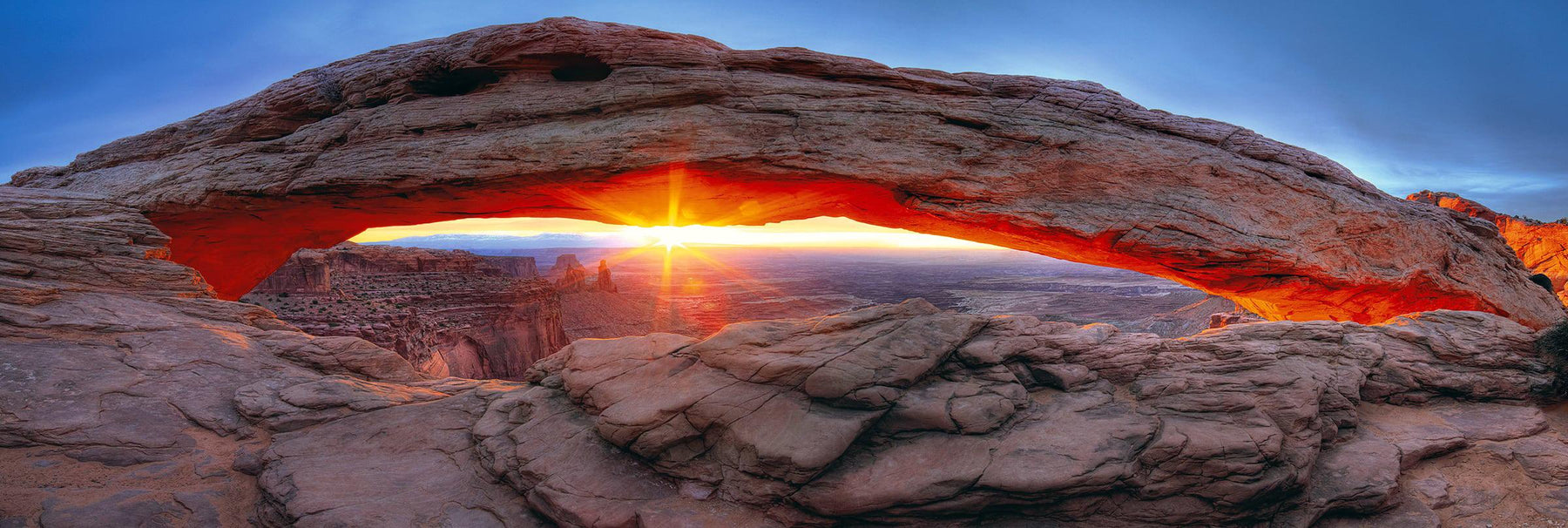 Sunburst shining through the stone arch and onto the rock valley of Canyonlands National Park Utah