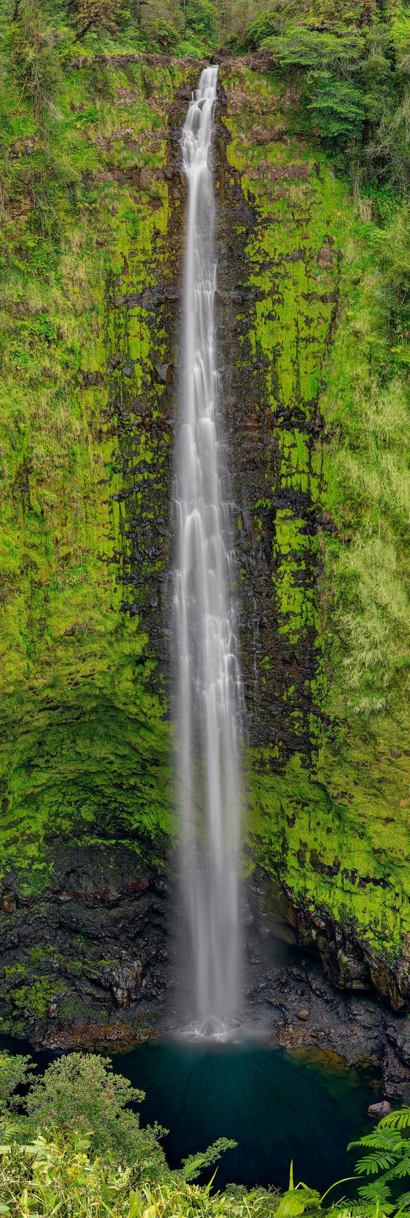 Waterfall pouring down a tall moss covered black rock cliff into a water hole below