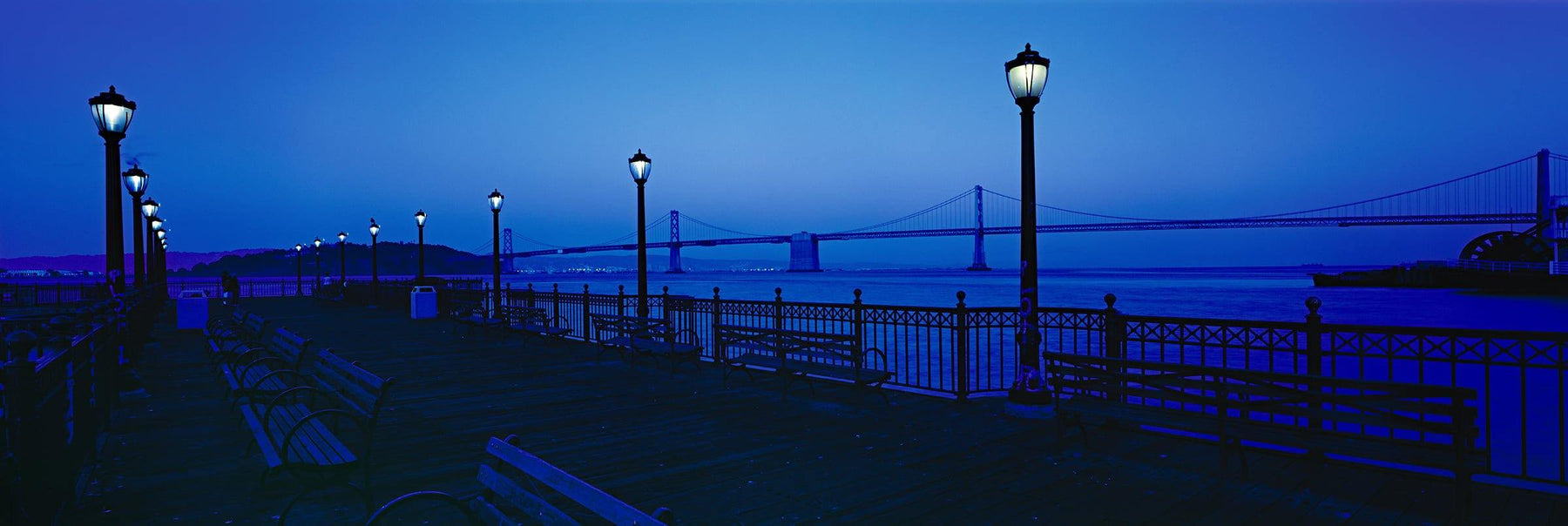 Wooden pier with antique lamp posts and benches at night in the San Francisco Bay