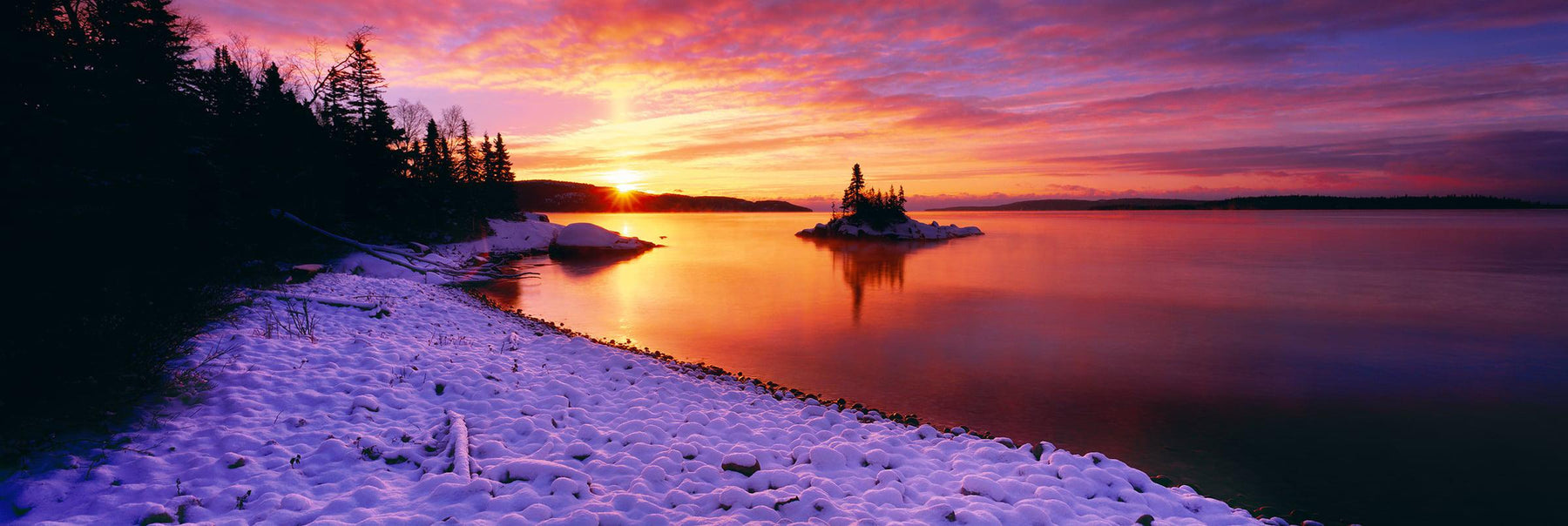 Snow covered beach of Lake Superior Minnesota lined by tree silhouettes at sunrise