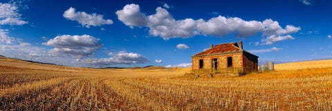 Sandstone shack in a cut wheat field in the outback of Burra Australia with puffy white clouds overhead in a blue sky