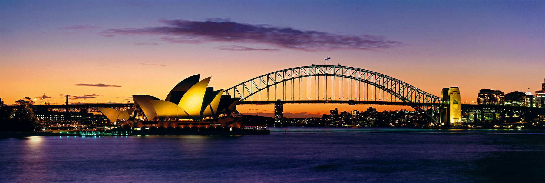 Sydney Harbor Bridge stretching over the harbor to the Sydney Opera House at sunset