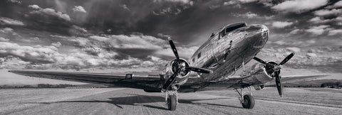 Black and white DC-3 airplane on a grass runway in Portland Oregon under a cloud filled sky