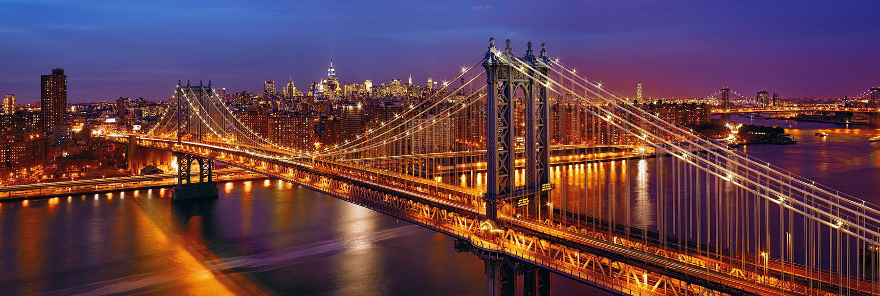 Manhattan Bridge lit up at night overlooking the glow of New York City in the distance