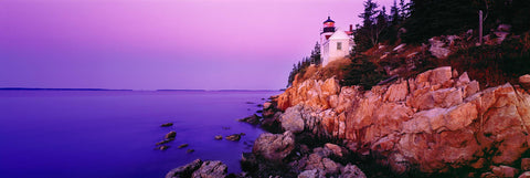 Bass Harbor Head Lighthouse off the edge of a rock cliff and the forest of Acadia National Park during sunrise