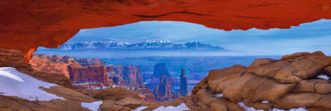 Snow covered rock arch overlooking the buttes and mountains of Canyonlands 