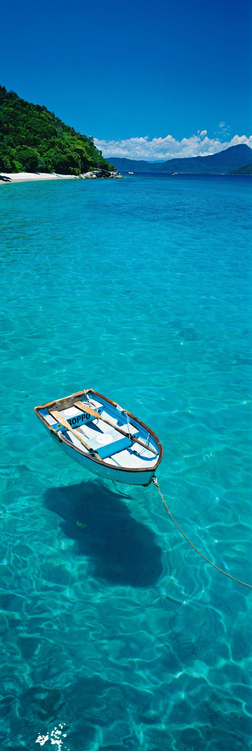 Rowboat floating on the turquoise waters in front of the tree filled Fitzroy Island Australia