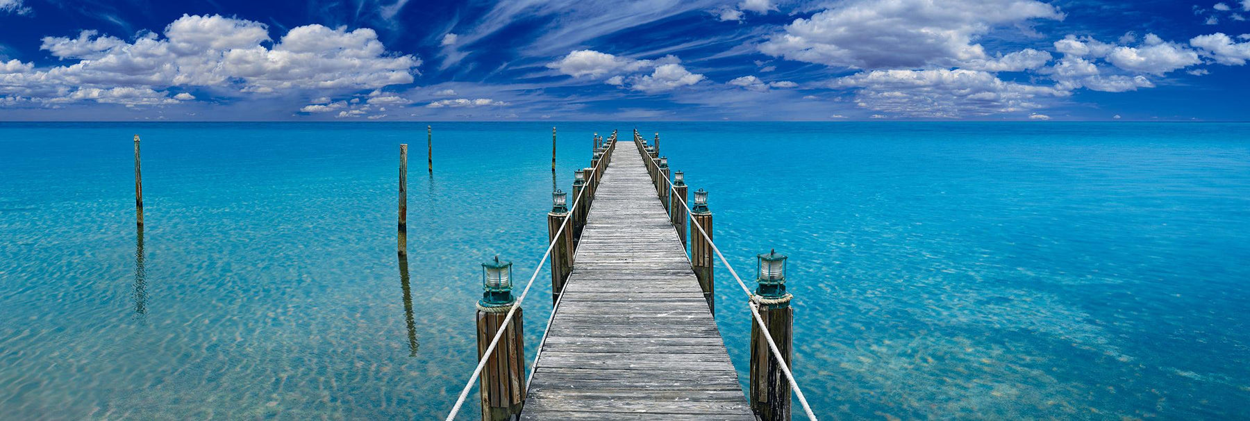 Old wooden jetty with white rope and lanterns leading over a turquoise ocean in Key West Florida