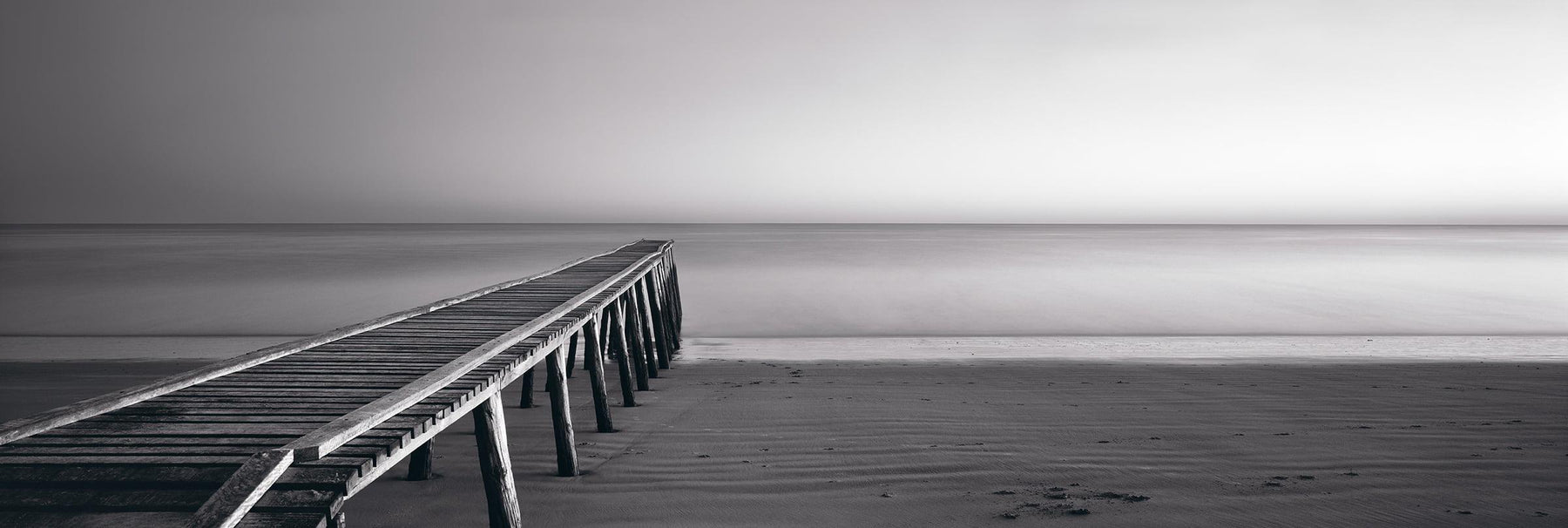 Black and white old wooden jetty leading across the sandy beach and into the ocean in Queensland Australia