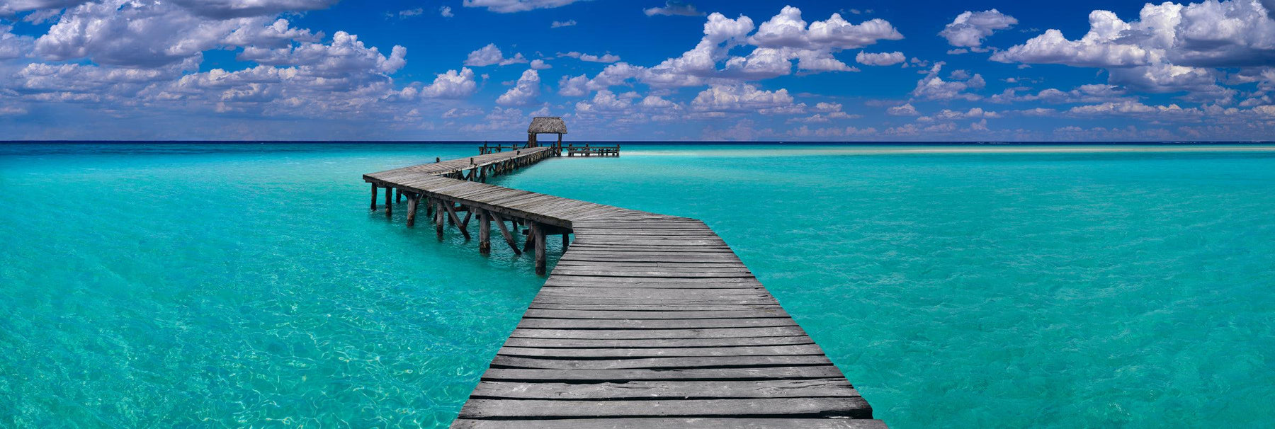 Old wooden jetty leading over the turquoise ocean out to a sand bay below a cloud filled sky